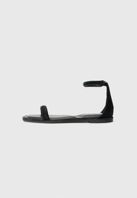 Čierne sandále s minimalistickým dizajnom, vybavené plochou podrážkou a úzkym remienkom okolo členku. Hladká textúra a otvorený dizajn na prednej časti zvyšujú priedušnosť.