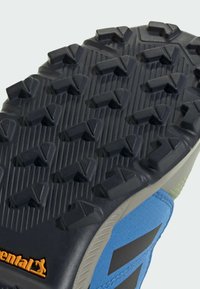 Η σόλα ενός μπλε και μαύρου αθλητικού παπουτσιού με βαθιές προεξοχές για καλύτερη πρόσφυση. Περιλαμβάνει υφές και το λογότυπο Continental σε πορτοκαλί.