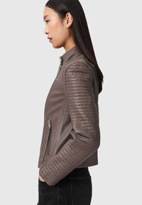 Braune Lederjacke mit tailliertem Schnitt, gesteppte texturierte Ärmel, Reißverschluss und Seitentaschen. Insgesamt glatte Oberfläche.