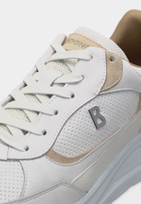 Λευκό αθλητικό παπούτσι με μπεζ σουέντ λεπτομέρειες, διάτρητη πλαϊνή επιφάνεια, λευκά κορδόνια και μεταλλικό λογότυπο "B" στην εξωτερική πλευρά.