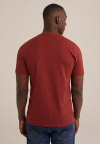 Rdeča kratka majica iz mehkega bombaža z običajnim okroglim ovratnikom in preprosto, gladko teksturo na hrbtni strani.