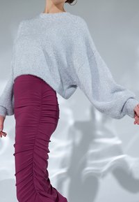 Světle modrý, třpytivý oversized svetr s kleslými rameny, který je spárován s přiléhavou, řasenou sukní v barvě švestky. Měkké textury a kontrastní tvary.