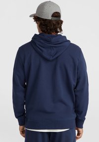 Navy blue cotton hoodie with a large hood, ribbed cuffs, and hem. Worn with a gray cap, viewed from the back, displaying a simple design.