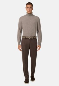 Pull à col roulé en tissu gris clair, ceinture tressée marron, pantalon marron et chaussures marron foncé avec une semelle blanche.