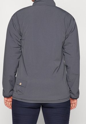 Personne portant une veste gris foncé avec une poche à pression sur le bas du dos, associée à un pantalon foncé, dos face à la caméra.