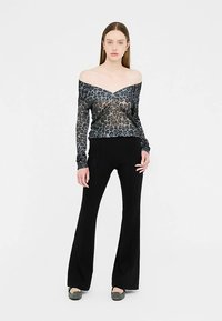 Schwarze Schlaghosen kombiniert mit einem halbtransparenten, schulterfreien Oberteil mit Leopardenmuster in Grautönen und Schwarz, das ein strukturiertes Design zeigt.