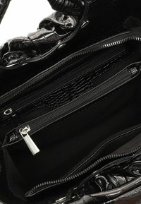 Czarna torebka z błyszczącą, tłoczoną teksturą krokodyla. Wnętrze wyposażone w wiele kieszeni na zamek błyskawiczny oraz gładką, miękką podszewkę.