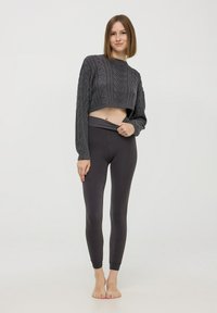 Szary sweter o splocie warkoczowym, krótki, z długimi rękawami, w połączeniu z nogawicami o wysokim stanie w ciemnym kolorze. Nogawice są gładkie z dopasowanymi mankietami.