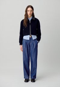 Chaqueta corta de color marino con cuello de cuero, combinada con una camisa a rayas azul claro y pantalones de mezclilla holgados. Unos zapatos negros completan el conjunto.