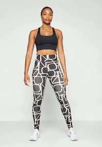Reggiseno sportivo nero e leggings a vita alta con un motivo geometrico crema, realizzati in tessuto elastico, adatti per l'abbigliamento sportivo.