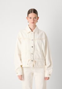 Kremfarget denimjakke med knappprofiler, to store brystlommer og justerbar snøring i falden. Har klassisk krage og avslappet passform.