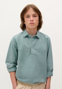 Chemise à col long à manches longues en teal clair avec patte de boutonnage et poignets retroussés ; présente un petit logo brodé sur la poitrine.