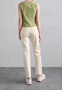 Grön ärmlös topp med en figurnära design, kombinerad med krämfärgade raka byxor och grå klackar med dekorativ sömnad.