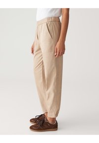 Pantalon beige décontracté avec taille élastique, poches latérales et jambes fuselées. Associés à des baskets marron avec lacets et finition texturée.