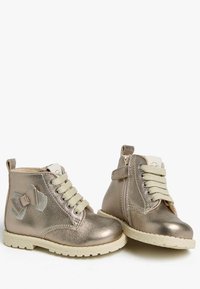 Metallisch goldene Knöchelstiefel mit glänzender Oberfläche, Schnürsenkeln, einem seitlichen Reißverschluss und einer dekorativen Schleife auf einer Seite. Strukturierte Gummisohle.