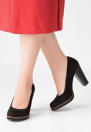 Chaussures à talons hauts en daim noir avec un bout arrondi et une plateforme texturée. Le talon est de forme bloc avec une finition imitant le bois.