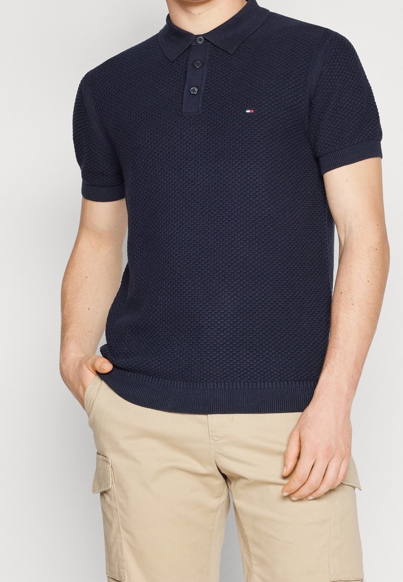 Marineblauw gebreid poloshirt met een gestructureerd ontwerp, voorzien van een effen kraag, drieknopenbies en geborduurd logo op de borst.
