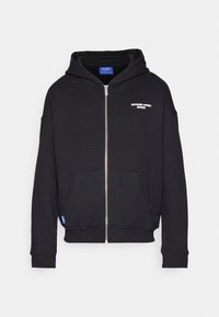 Black zip-up hoodie made of soft fabric; features a front pocket, ribbed cuffs, and a hood, with white text printed on the left chest.