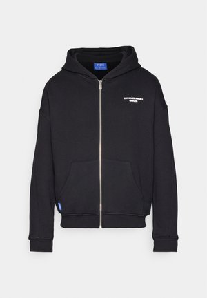 Juodas zip-up kapšas, pagamintas iš minkštos medžiagos; turi priekinį kišenę, gumuotus rankogalius ir gobtuvą, su balta tekstu, atspausdintu kairiajame krūtinės kampelyje.