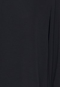 Black fabric with a soft, textured surface. Lightweight and flowy design; features a loose fit and subtle draping details.