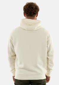 Sweatshirt à capuche en écru, avec un tissu texturé, des poignets et un ourlet côtelés. La vue arrière montre une coupe décontractée et une capuche spacieuse.