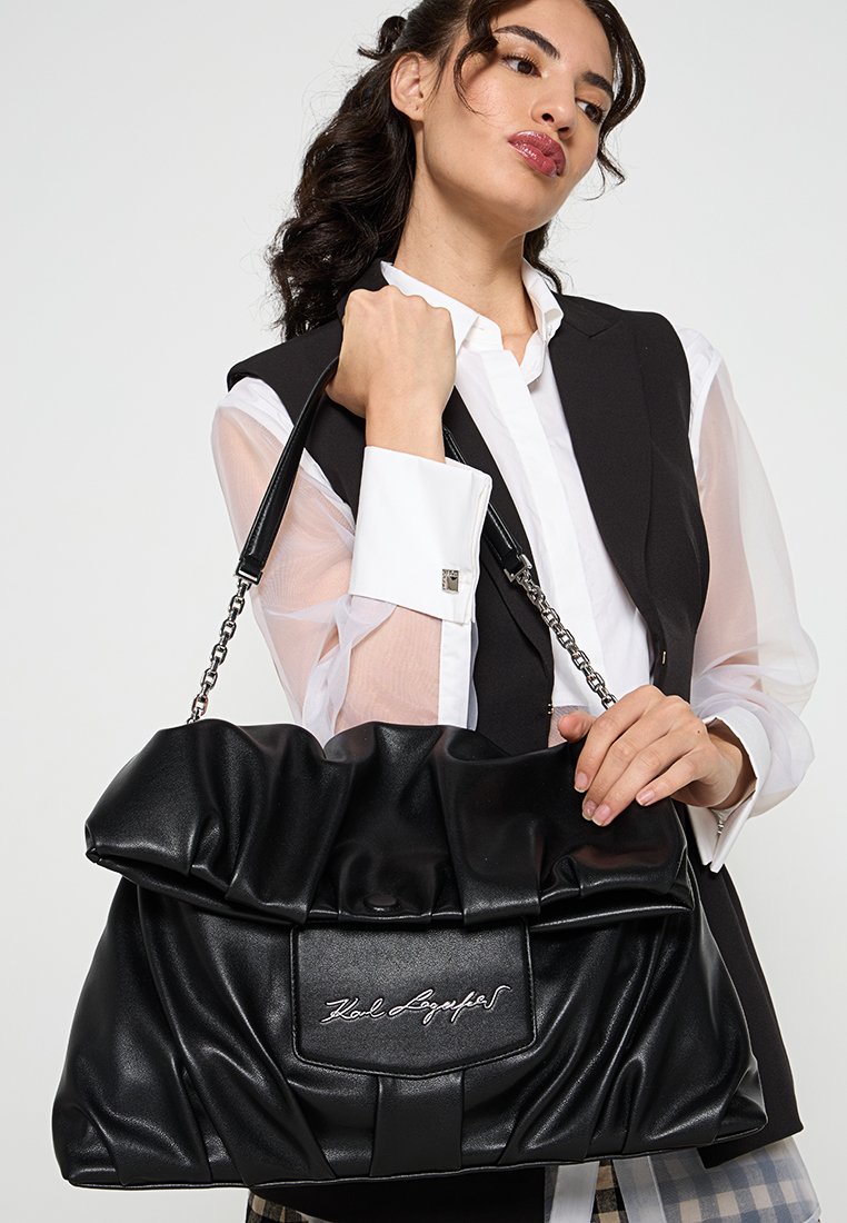 Sac à main en simili cuir noir avec un design matelassé, bandoulière en chaîne et détail de logo. Texture douce avec une forme structurée.