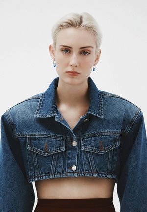 Chaqueta de mezclilla recortada en azul medio con un cuello clásico, dos bolsillos en el pecho, botones plateados y costuras naranjas en contraste.