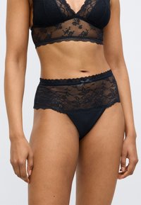 Černá krajková podprsenka a odpovídající kalhotky s vysokým pasem, zdobené květinovými vzory, vroubkovanými okraji, hladkou látkou a malým mašličkovým doplňkem.