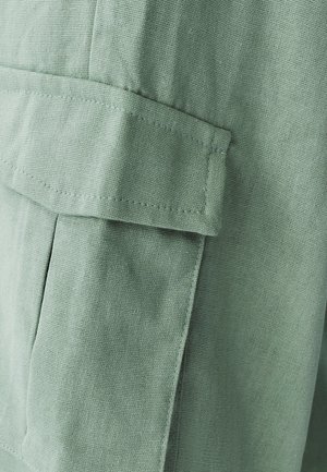 Hellgrüner Stoff mit strukturierter Oberfläche, versehen mit einer aufgesetzten Tasche und sauberem, präzisem Stich entlang der Kanten für Langlebigkeit.