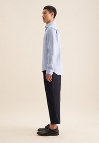 Lichtblauwe linnen overhemd met lange mouwen en een button-down kraag, gecombineerd met donkere cropped broeken en zwarte leren schoenen.