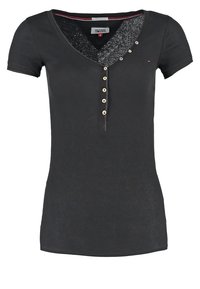 Camiseta ajustada de manga corta tipo Henley en negro con cuello en V, seis botones frontales, pequeño logo de Tommy Hilfiger en el pecho y etiqueta interior visible.