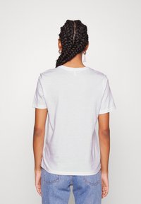 Camiseta blanca de algodón con mangas cortas y cuello redondo, con una textura suave. Combinada con unos jeans de mezclilla de color azul claro.