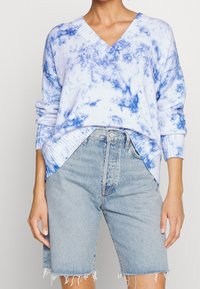 Ljusblått stickat tröja med batikeffekt, med V-ringning och ribbade ärmslut, tillsammans med ljusa denimshorts med fransade kanter.