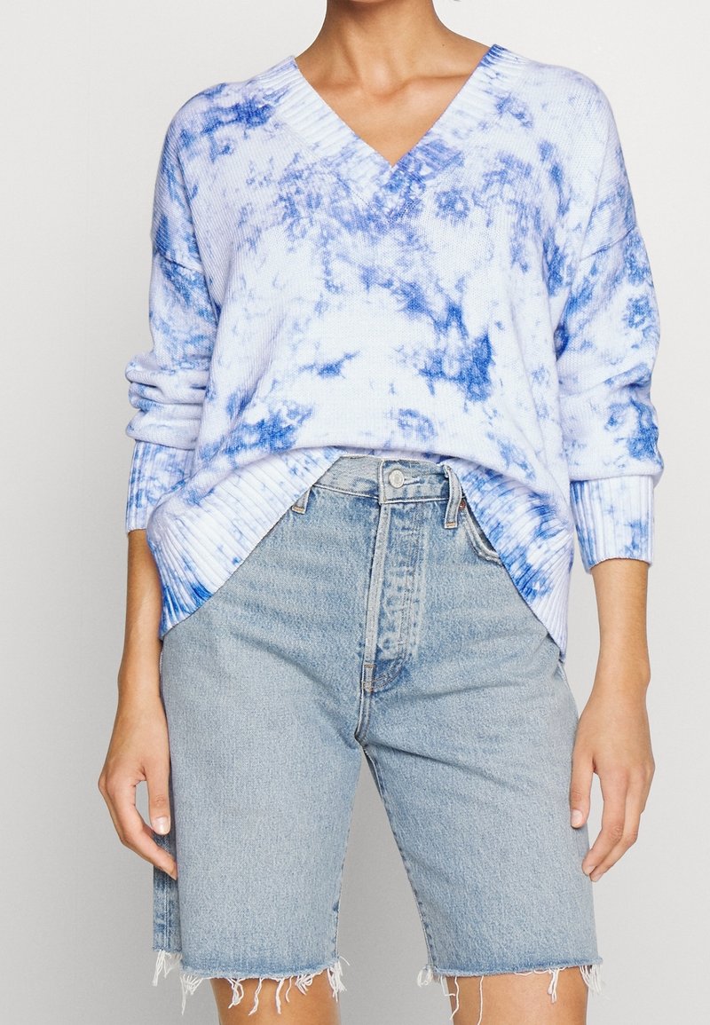 Ljusblått stickat tröja med batikeffekt, med V-ringning och ribbade ärmslut, tillsammans med ljusa denimshorts med fransade kanter.