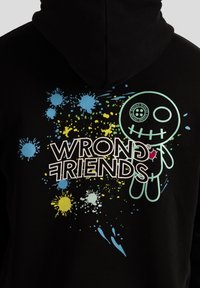 Felpa nera con cappuccio caratterizzata da un design grafico con macchie di vernice colorate in blu, giallo e verde, e un personaggio stilizzato con un cuore.