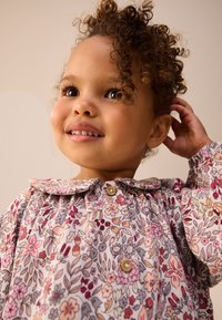 Virágmintás ruha rózsaszín, piros és kék virágokkal világos alapon. Kerekített gallérral és két gombbal a nyaknál.