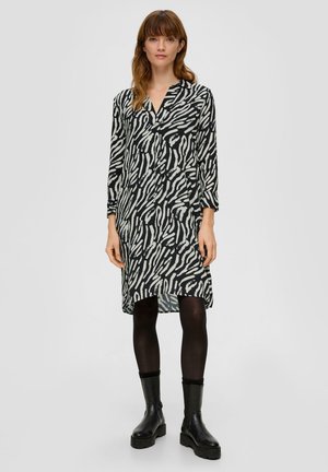 Zwart-wit gestreepte jurk van lichtgewicht stof, met een V-hals, lange mouwen en een relaxed fit, gecombineerd met zwarte enkellaarzen.