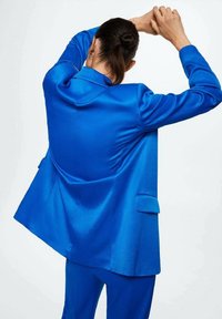 Bright blue satin blazer with structured design, visible shoulder pads, and patch pockets, shown from the back with arms raised.