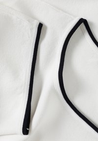 White fabric with a soft texture, featuring black trim along the edges and neck lines. The design includes overlapping layers.