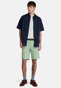 Koszula na krótki rękaw w granatowym kolorze, zapinana na guziki, noszona na białym t-shircie, w połączeniu z miętowymi szortami, szarymi skarpetkami i brązowymi butami.