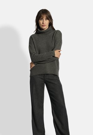 Grå strikket turtleneck trøje med løs pasform, der har ribbede manchetter og kant, parret med løse sorte bukser. Ingen yderligere mønstre eller detaljer.