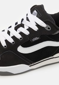 Czarny zamszowy i siateczkowy sneaker z białymi sznurowadłami, z białym bocznym paskiem, naszywką z logo na języku i czarną gumową podeszwą.