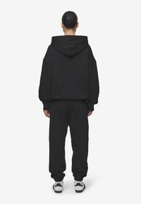 Sudadera negra de gran tamaño con capucha, combinada con pantalones de chándal negros a juego. La tela parece suave, con puños y tobillos acanalados.