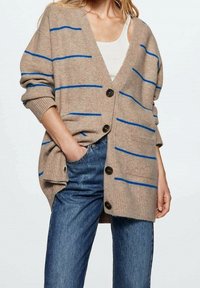 Beżowy kardigan z niebieskimi paskami, o luźnym kroju, z długimi rękawami i dużymi czarnymi guzikami. Tkanina wydaje się miękka, z prążkowanymi akcentami.