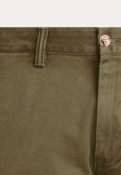 Primer plano de la cintura de pantalones verde caqui con un botón de metal y detalle de trabilla en una tela lisa.