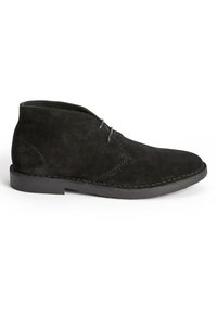 Botas de ante negras hasta el tobillo con punta redondeada, dos ojales para los cordones y una suela de goma plana con costuras visibles a lo largo de los bordes.