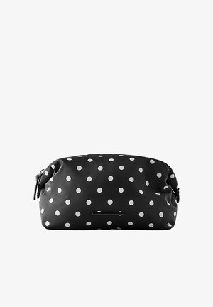 Trousse de maquillage rectangulaire noire à pois blancs avec fermeture éclair sur fond blanc.