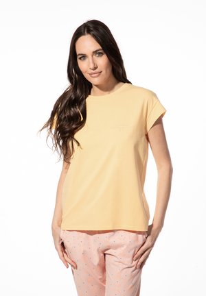 Geel t-shirt met korte mouwen van zachte stof, voorzien van een ronde halslijn en subtiele borduursels op de voorkant. Gecombineerd met een roze broek met patroon.