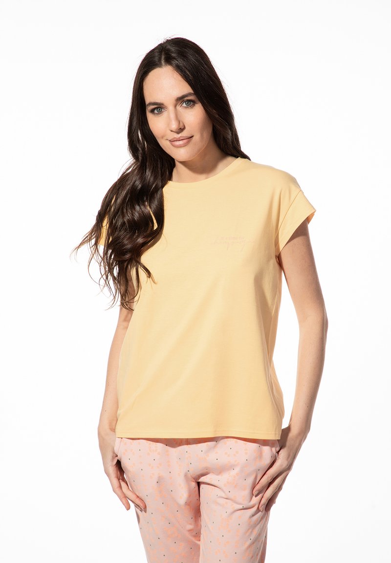 Geel t-shirt met korte mouwen van zachte stof, voorzien van een ronde halslijn en subtiele borduursels op de voorkant. Gecombineerd met een roze broek met patroon.