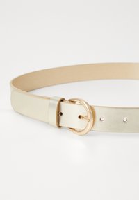 Ceinture métallique dorée avec une texture lisse, dotée d'une boucle circulaire en or et d'un trou d'ajustement. Design plat, adaptée à divers vêtements.